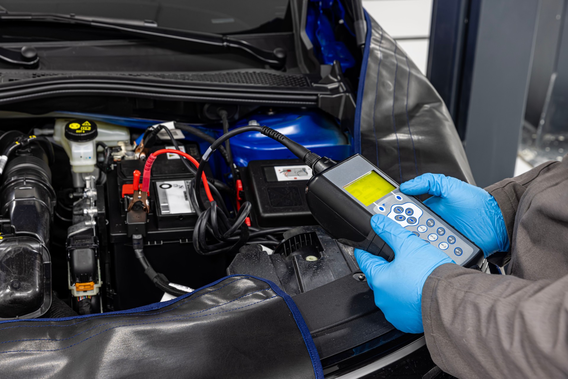 Car master mechanic checking and testing automotive battery with digital electronic battery tester and analyzer in auto vehicle workshop.